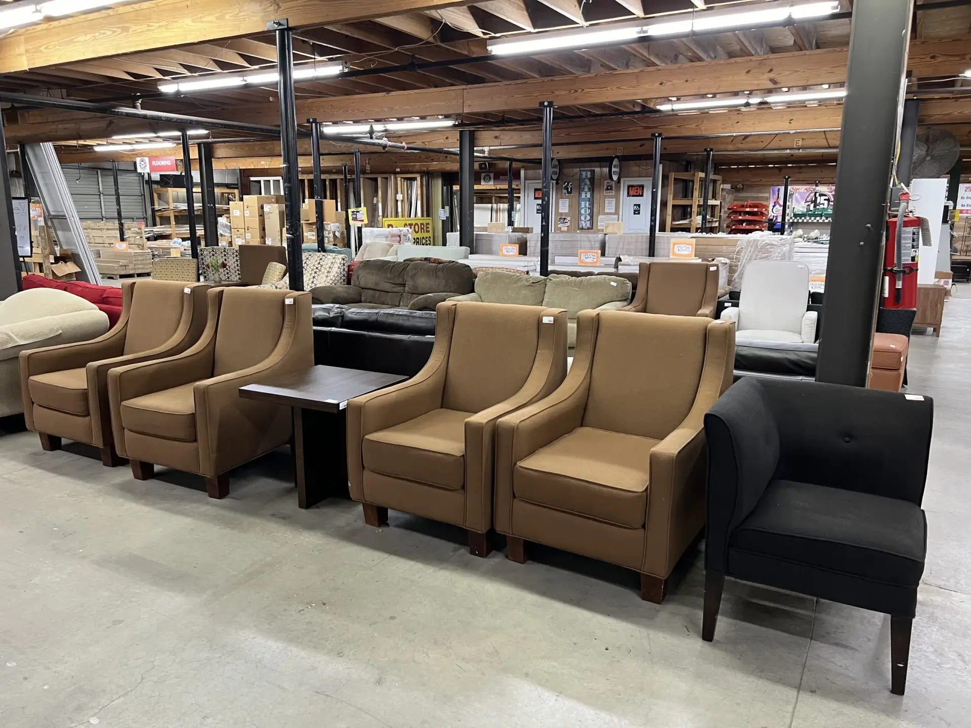 Rows of upholstered armchairs, sofas, and accent tables displayed on a concrete floor inside the spacious, bright furniture showroom at The Re-Store Warehouse.
