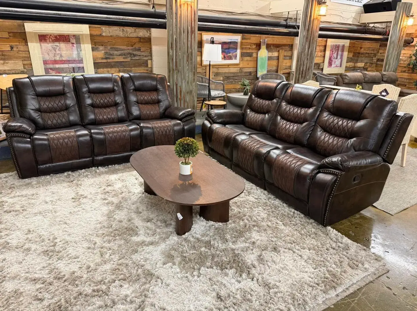 Matching dark brown leather reclining sofas with two-tone diamond stitching around an oval wooden coffee table on a shag rug at Re-Store Warehouse