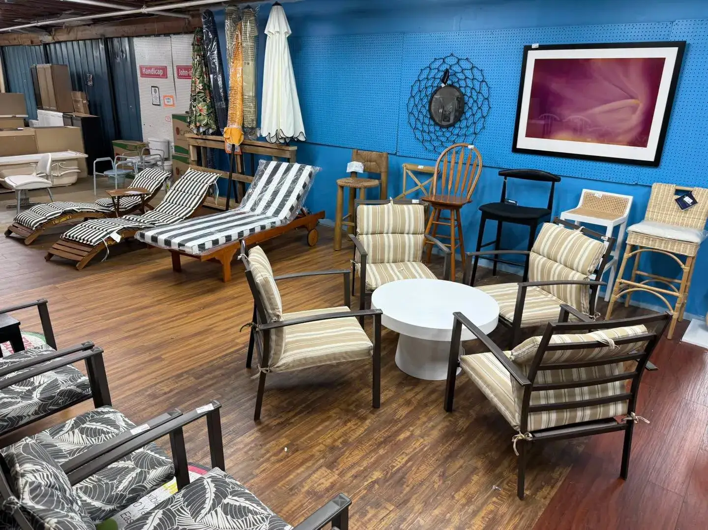Display of outdoor patio furniture including striped loungers, metal armchairs with cushions, barstools, and umbrellas at Re-Store Warehouse
