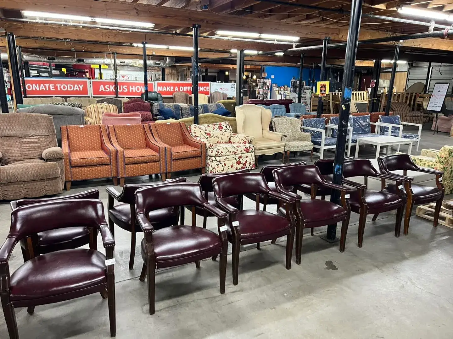 Burgundy leather office armchairs with nailhead trim and dark wooden legs on a concrete floor in a Habitat for Humanity ReStore warehouse.