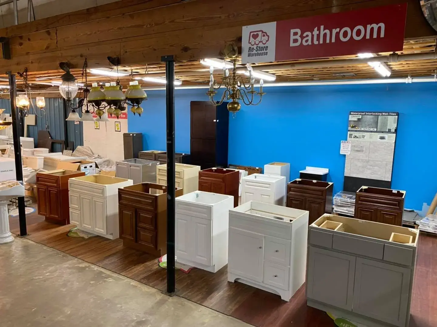 Multiple wooden and painted bathroom vanity cabinets without counter tops arranged on display beneath a red Bathroom signage banner inside Re-Store Warehouse.